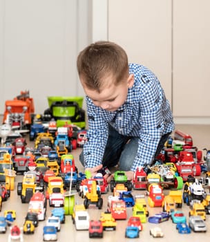 Concept of children's toys. A little boy, 4 years old, enthusiastically plays, sitting on the floor, with multi-colored small and large cars in the children's room. Soft focus