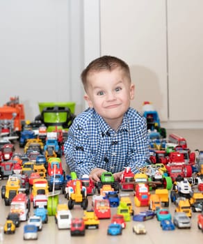 Concept of children's toys. A little boy, 4 years old, plays happily, lying on the floor, with colorful small and large cars in the children's room. Soft focus.