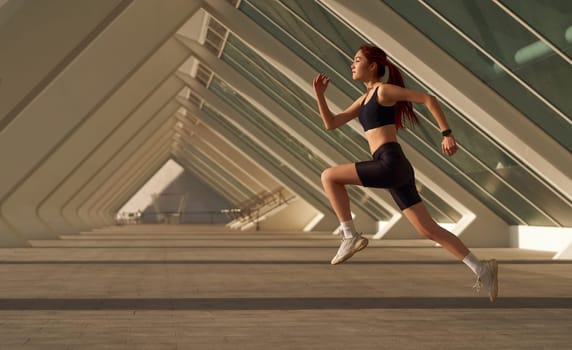 Young woman in sportswear is running on modern buildings background. Active lifestyle concept