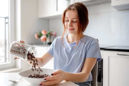 Sweet Teenage Girl Pours Cereal Into Plate For Breakfast In Kitchen