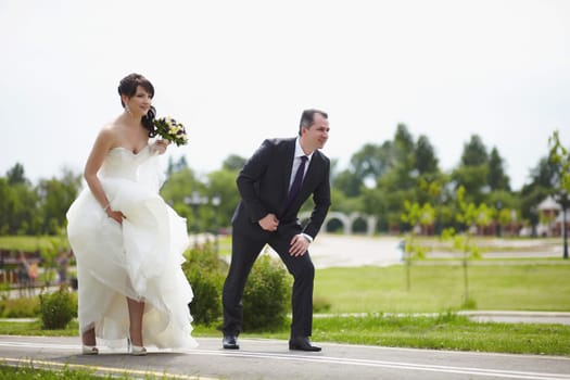 The bride in a white dress and the groom stand at the start before running on an asphalt track