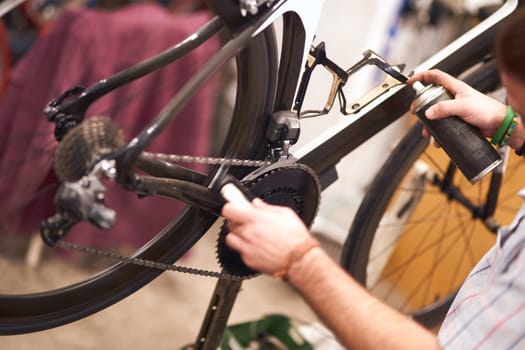 Close up of repairman is holding spray lubricant in his hand to lubricate the bike chain