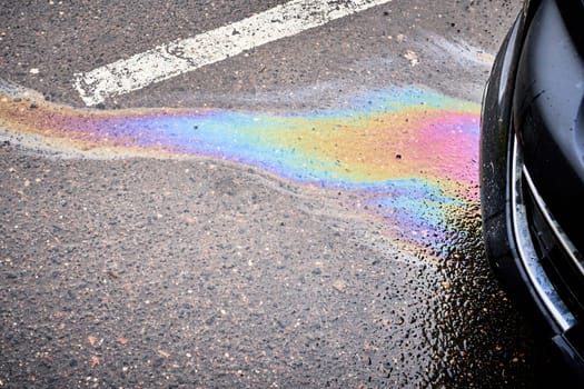 The wet asphalt in a parking lot near a hypermarket is stained with gasoline and oil spill