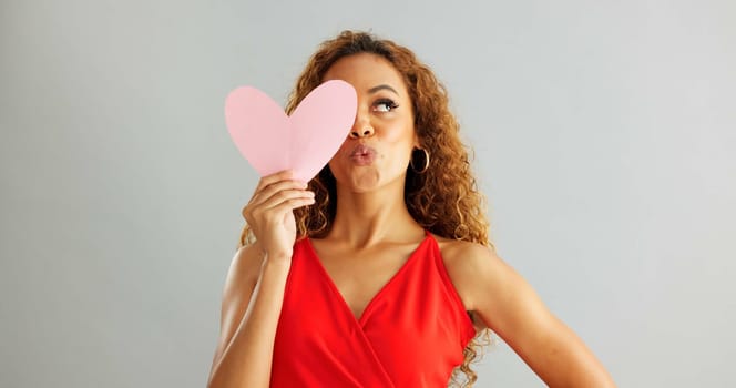 Woman, love and kiss face with paper heart for opinion, romance or thinking with ideas on grey background. Face, emoji and female person with happiness for kindness, vote or support on valentines day.