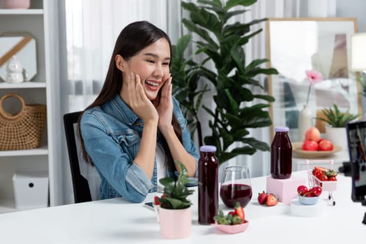 Smiling young beautiful Asian reviewing tasty mixed strawberry and cherry juice detox drinks, showing healthy product to promote for special promotion selling on social media online record. Stratagem.