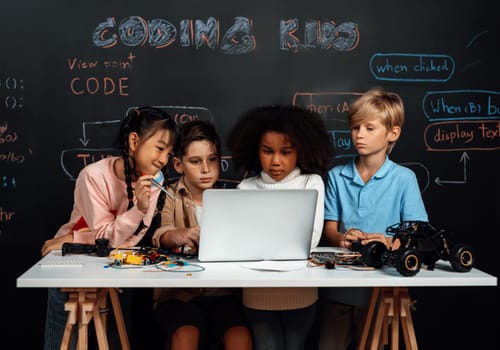 In classroom student in STEM class learning about coding robotics car. Children watching at laptop and thinking. Boys and girl looking seriously, but only child in pink cloth look funny. Erudition.