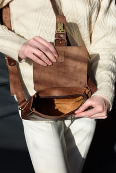 beautiful woman posing with a small brown bag near grey wall. Model wearing stylish white sweater and classic trousers