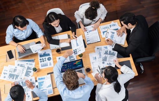 Wide top view of diverse group of business analyst team analyzing financial data report paper on meeting table. Chart and graph dashboard by business intelligence analysis. Meticulous