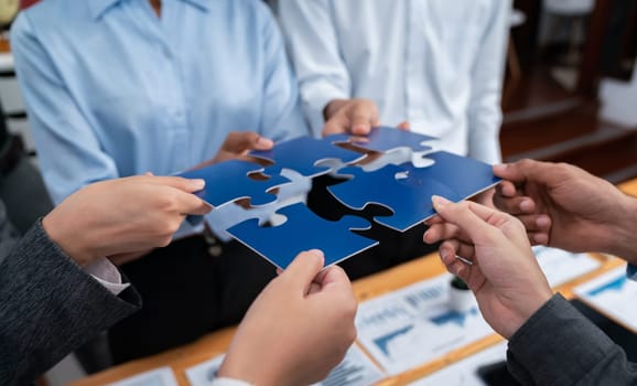 Corporate officer worker collaborate in office, connecting puzzle pieces with report paper on table as partnership and teamwork. Unity and synergy in business concept by merging jigsaw puzzle. Concord