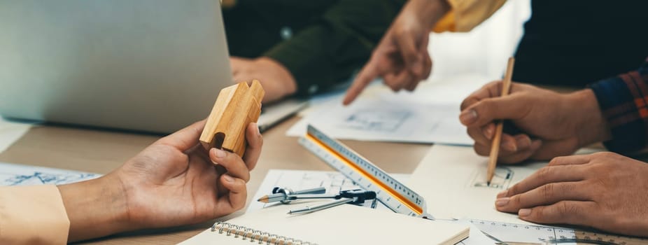 Professional architect team discussion about architectural project on meeting table with blueprint and wooden block scatter around at modern office. Closeup. Focus on hand. Delineation.