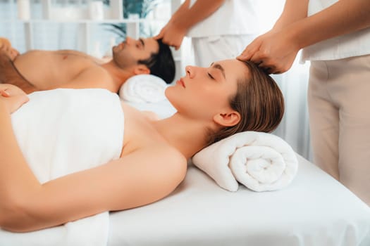 Caucasian couple enjoying relaxing anti-stress head massage and pampering facial beauty skin recreation leisure in dayspa modern light ambient at luxury resort or hotel spa salon. Quiescent