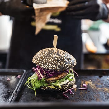 Chef making healthy vegetarian salmon burgers outdoor on open kitchen, odprta kuhna, international food festival event. Street food ready to be served on a food stall.