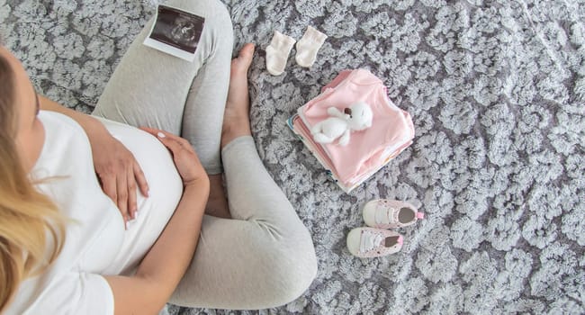 A pregnant woman collects baby things. Selective focus. Home.