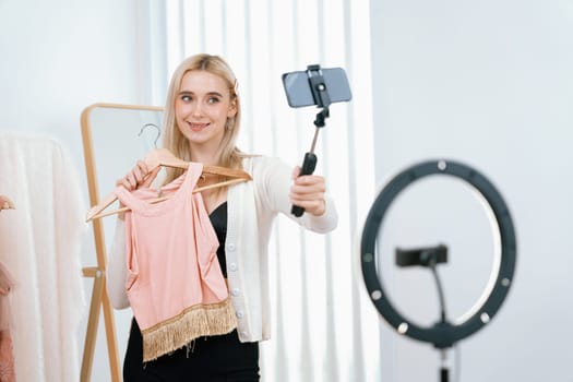 Young social medial content creator woman make fashion video. Blogger smiles to camera and light ring while making persuasive online clothing sell vlog to audience or follower. Blithe