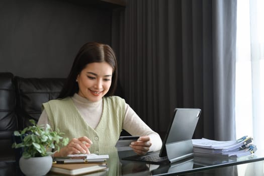 Millennial woman holding credit card and calculating monthly expenses at home.