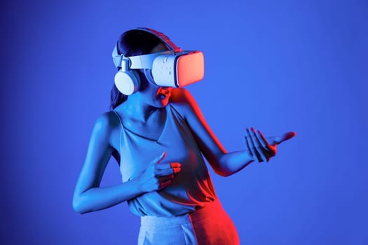 Smart female standing wearing VR headset connecting metaverse, future cyberspace community technology. Elegant woman using hands commanding virtual gun seriously playing shooting games. Hallucination.