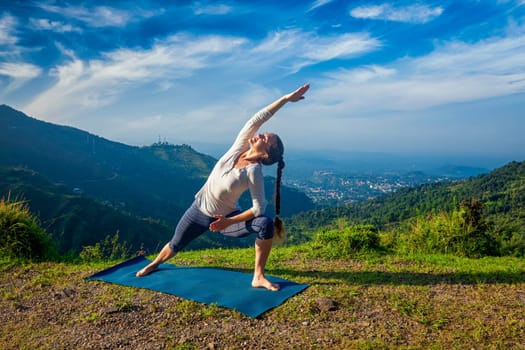 Woman practices yoga asana Utthita Parsvakonasana - extended side angle pose outdoors in mountains in the morning