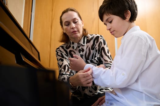 Pianist woman rolls up the sleeves on her student's shirt, prepares him for individual piano lesson. Musical education and artistic development of kids. Learning playing piano