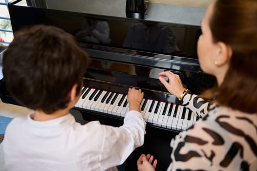 View from above of Caucasian adorable teen boy enjoying playing grand piano at home, creating music and song, performing soundtrack on the pianoforte, composing a melody during music lesson.