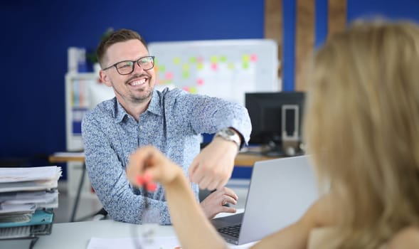 Cheerful man in glasses show client watch on his hand at workplace. Visitor sit opposite employee.