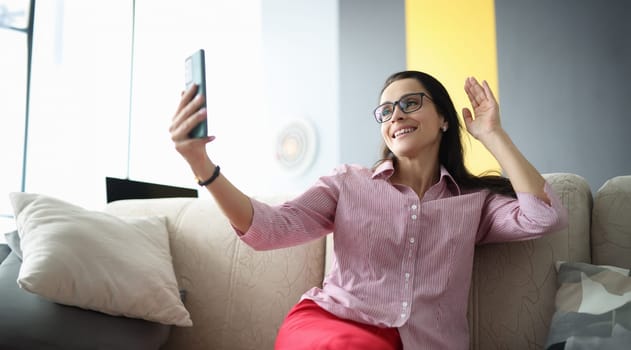 Beautiful woman in glasses wave hello on internet connection. Person talk online through phone at home.