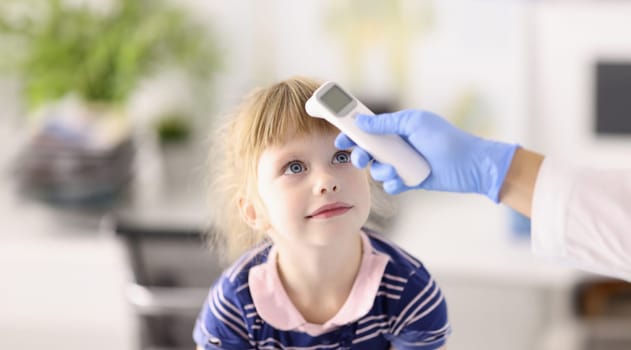 Pediatrician doctor in rubber glove measures temperature of child with infrared thermometer portrait. Diagnosis and treatment of covid19 in children concept.