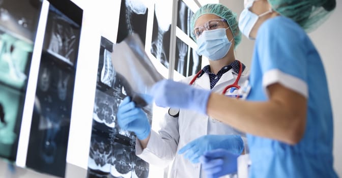 Two doctor in suits, medical gloves and protective masks hold X-ray photograph. Two women study results of internal examinations.