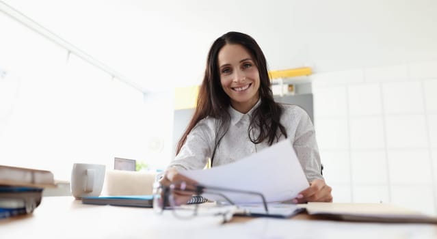 Beautiful and happy woman portrait in office. Worker hold sheet of paper with graphs in hands and smile.