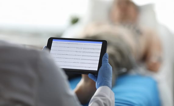 Close-up of medical worker holding modern technology tablet and examine heart rate. Patient on hospital bed under observation. Medicine healthcare and ecg concept
