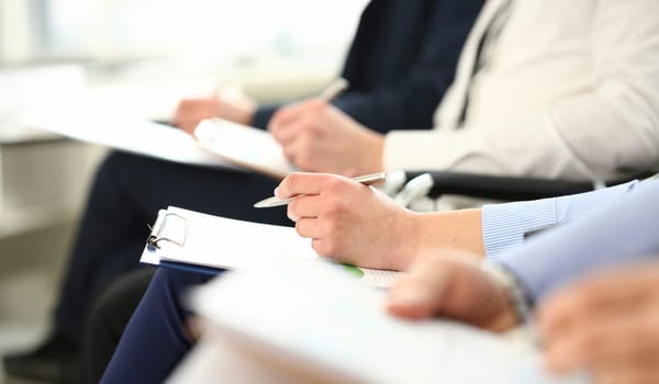 Bunch of people sitting in queue with clipboards and pens making some notes closeup