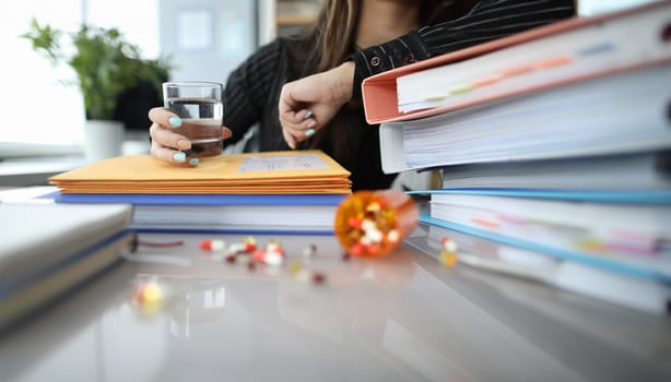 Close-up of female hand holding glass of water. Overworked worker taking medication on workplace. Soothing pills on table. Health care and medicine concept