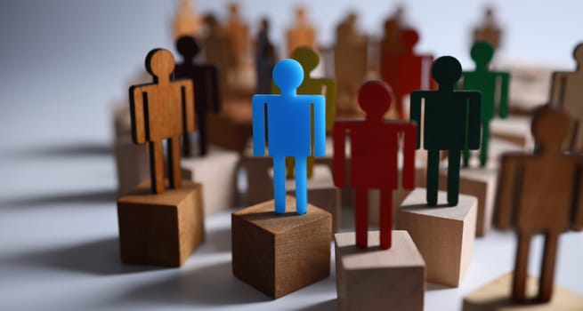 Close-up of colourful plastic figures standing on wooden blocks. Symbol of leadership and uniqueness. Business and success in career. Strategy and goal planning concept