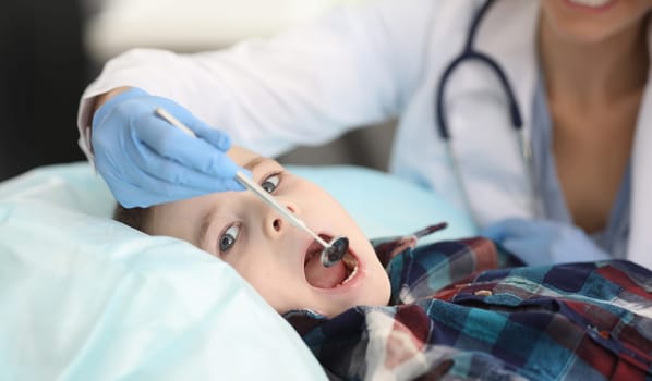 Close-up of boy laying on hospital bed on doctor appointment. Child opens mouth to checkup throat. Medical worker in uniform. Medicine and pediatrician concept