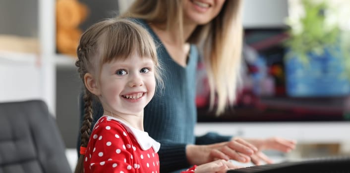 Mom teaches daughter to play electronic piano. Child remembers musical text. Example of cultural and polite behavior. School teachers will do their best. Girl has desire and ability for music