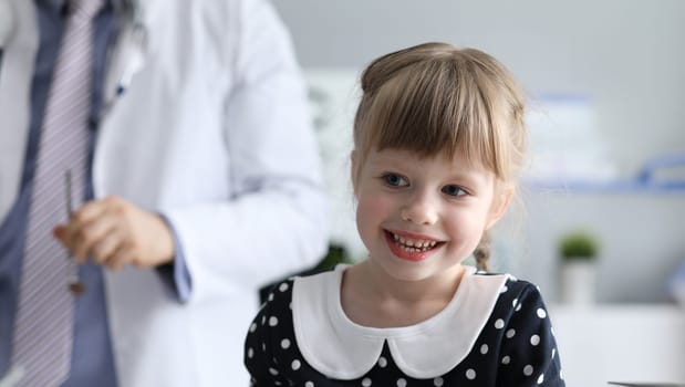 Healthy little girl is sitting in doctors office. Diagnosis and treatment diseases in children. Consultation with children specialist. Family doctor provides expert care in treatment