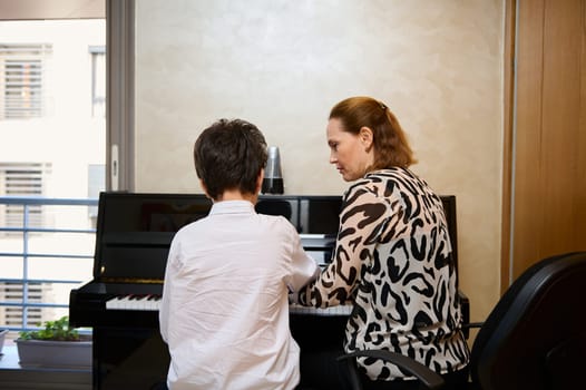 Rear view of a music teacher explaining piano lesson to her student during individual music lesson at home. Musical education and artistic development for young people and kids. Hobbies and leisure