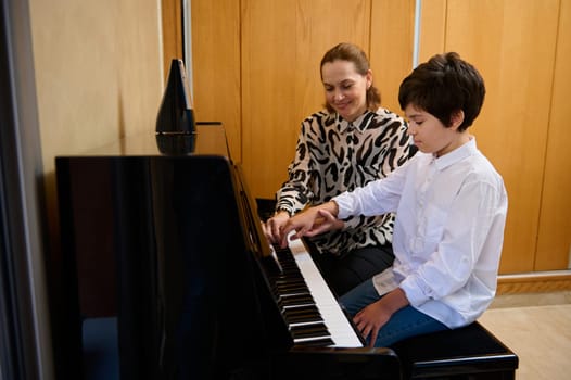 Authentic female music teacher explaining piano lesson to her student during individual music lesson at home. Musical education and artistic development for young people and kids. Hobbies and leisure