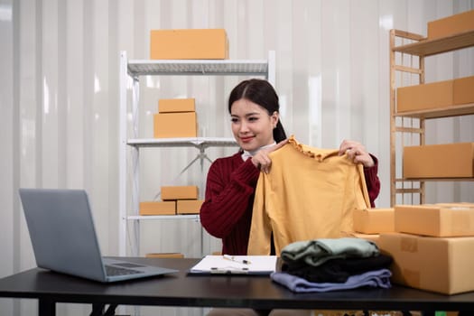 Woman asian online sell is using smartphone to live on vlog for introduce while review shirt collection selling online clothing on social media.