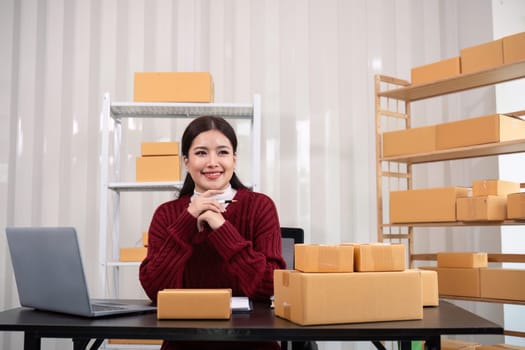 Young business woman asian working online ecommerce shopping at her shop. Young woman sell prepare parcel box of product for deliver to customer. Online selling.