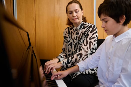 Teenager schoolboy playing piano with his teacher during individual music lesson at home. Musical education and artistic development for young people and kids. Hobbies and leisure