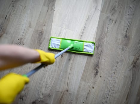 Male hand with yellow protective gloves hold green plastic mop close-up. Cleaning after repair concept