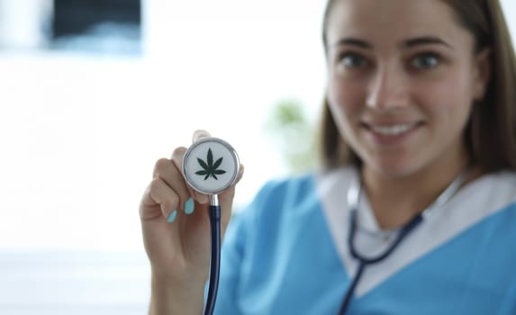 Close-up of female hand holding stethoscope with cannabis sign. Smiling doctor practitioner in medical gown. Medicine and healthcare. Medical marijuana concept