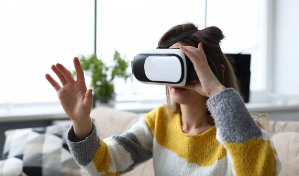 Girl sitting home looking through virtual glasses. Virtual reality simulates exposure and response to exposure, gaming. Young woman on sofa experiencing peace and positive emotions