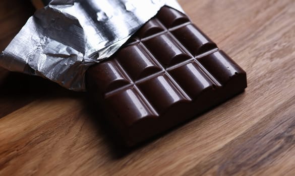 Close-up of dark chocolate bar in foil with open cover laying on wooden table. Unpacked sweets with nut. Calories and antioxidant. Sweet and yummy dessert concept