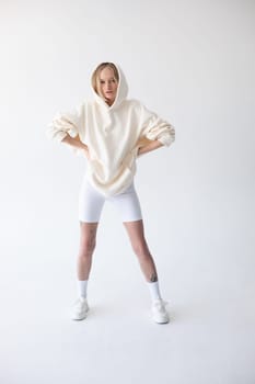 Beautiful blonde woman posing in white hoodie and leggings posing against white background. High quality photo