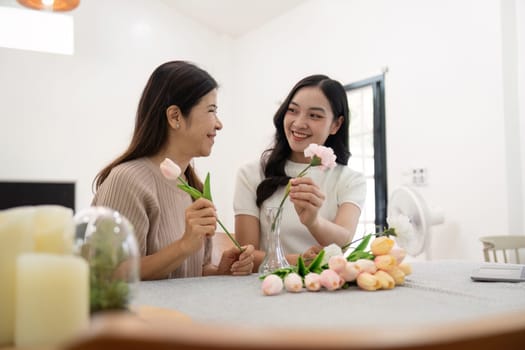 Senior mother and adult daughter happy on the table while arrange flowers in a vase together. Technology and lifestyle concept. Happy time together.