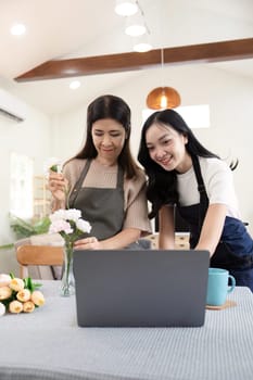 Senior mother and adult daughter happy on the table while arrange flowers in a vase together using laptop computer. lifestyle concept. Happy time together.