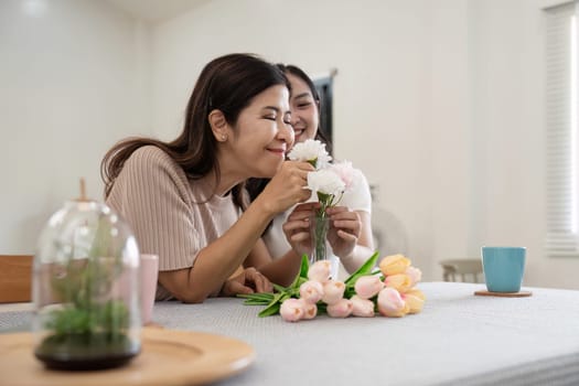 Senior mother and adult daughter happy on the table while arrange flowers in a vase together. Technology and lifestyle concept. Happy time together.