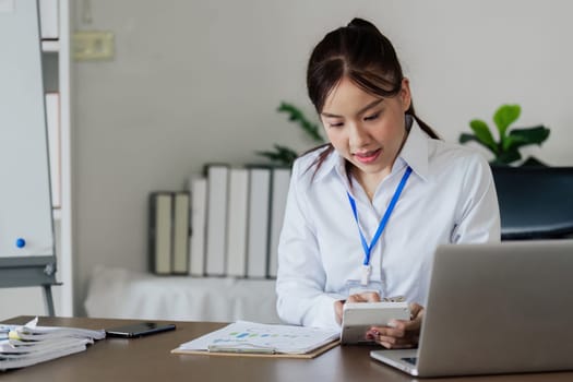 A woman is writing on a piece of paper with a pen. She is wearing a black suit and is sitting at a desk. The paper has a lot of numbers and calculations on it.