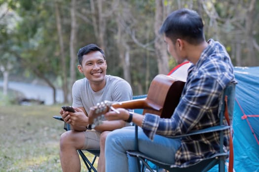 Young Asian homosexual couple camping on a picnic Play guitar together for a relaxing holiday..